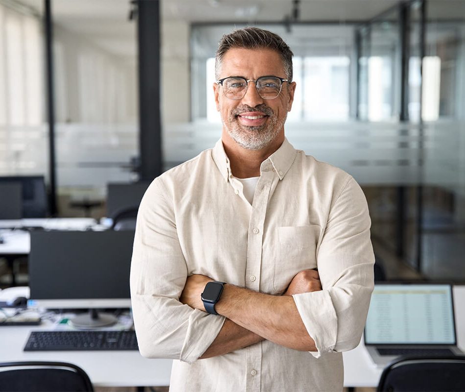 Handsome hispanic senior businessman with crossed arms smile at camera in office